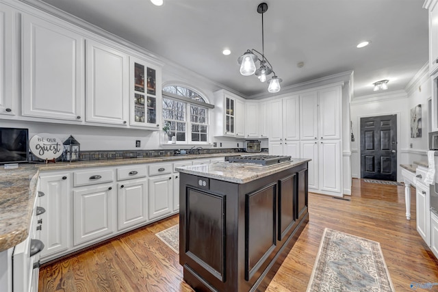 kitchen with white cabinetry, a center island, ornamental molding, light stone countertops, and decorative light fixtures