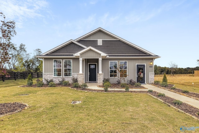 craftsman house with stone siding, fence, a front lawn, and board and batten siding