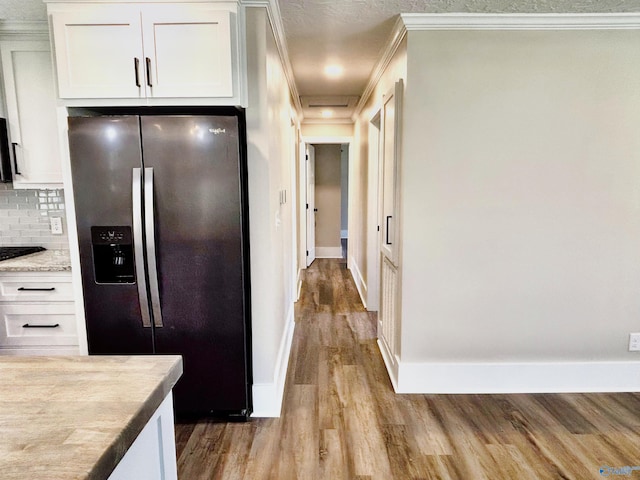 kitchen with stainless steel fridge, ornamental molding, backsplash, white cabinets, and wood finished floors