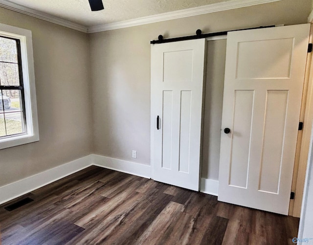 unfurnished bedroom with a barn door, dark wood-type flooring, multiple windows, and visible vents