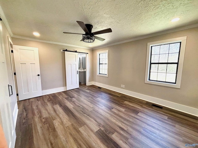 unfurnished bedroom with a barn door, baseboards, visible vents, ornamental molding, and dark wood-style flooring
