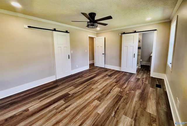 unfurnished bedroom featuring baseboards, a barn door, wood finished floors, and crown molding