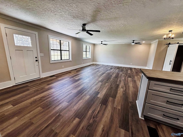 unfurnished living room featuring ornamental molding, dark wood-type flooring, a textured ceiling, a barn door, and ceiling fan