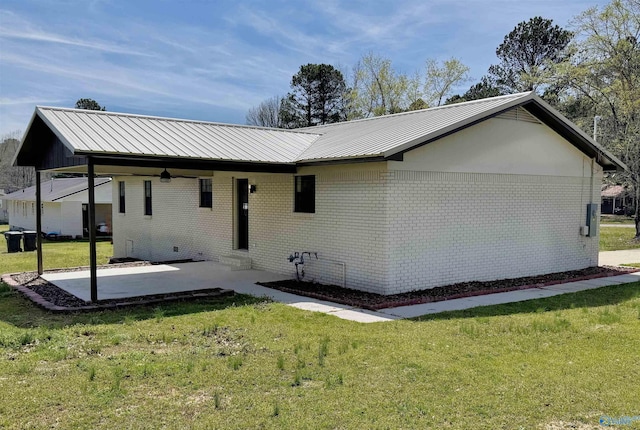 rear view of property featuring a lawn, metal roof, a patio area, and brick siding