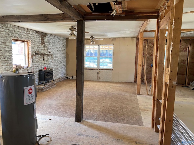 basement with a wood stove, a ceiling fan, a wealth of natural light, and electric water heater