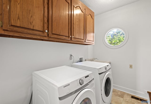 washroom with cabinets, washer and dryer, and a textured ceiling