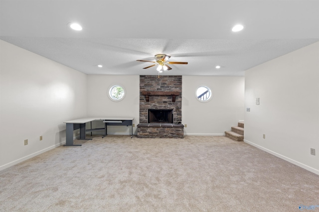 unfurnished living room featuring ceiling fan, a stone fireplace, light colored carpet, and a wealth of natural light