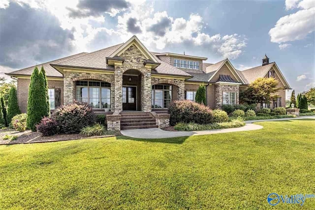 view of front of home featuring a shingled roof, a front yard, and stone siding