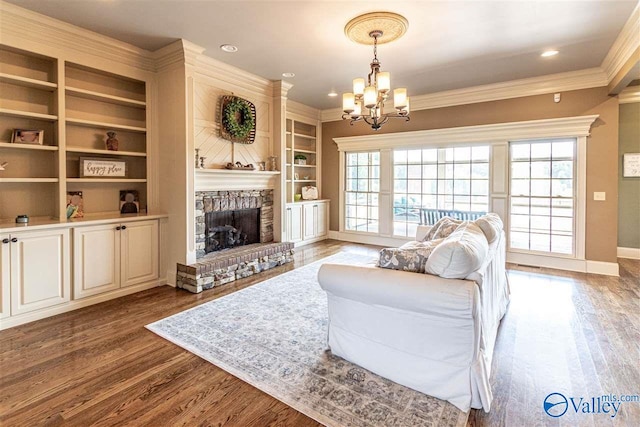 living room featuring a notable chandelier, a fireplace, wood finished floors, baseboards, and crown molding