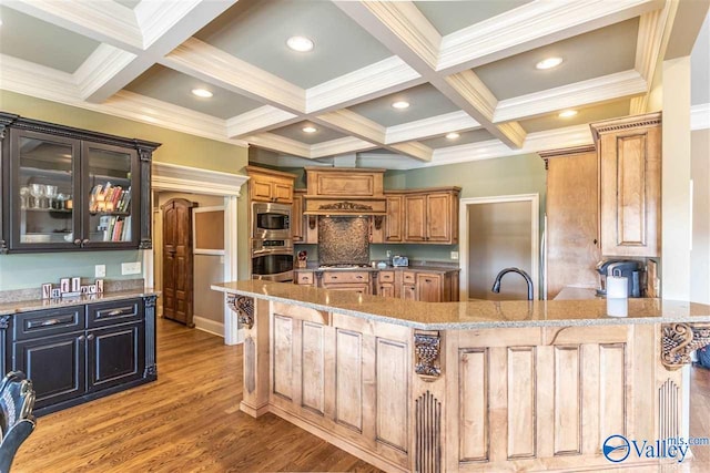 kitchen with stainless steel appliances, coffered ceiling, light stone counters, beamed ceiling, and a kitchen bar