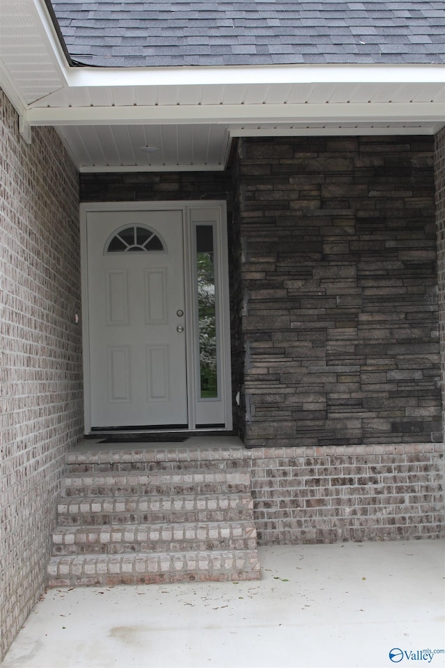 property entrance featuring a shingled roof and brick siding