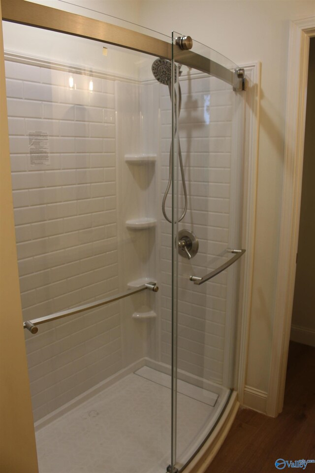 full bath featuring a shower stall, baseboards, and wood finished floors