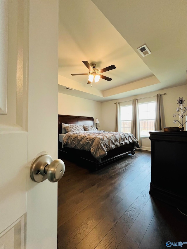 bedroom with ceiling fan, a raised ceiling, and dark wood-type flooring