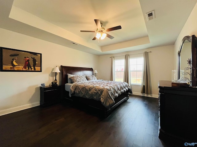 bedroom featuring ceiling fan, dark hardwood / wood-style floors, and a tray ceiling