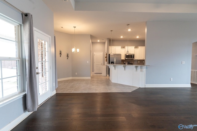 kitchen with hardwood / wood-style floors, hanging light fixtures, appliances with stainless steel finishes, white cabinetry, and a breakfast bar area