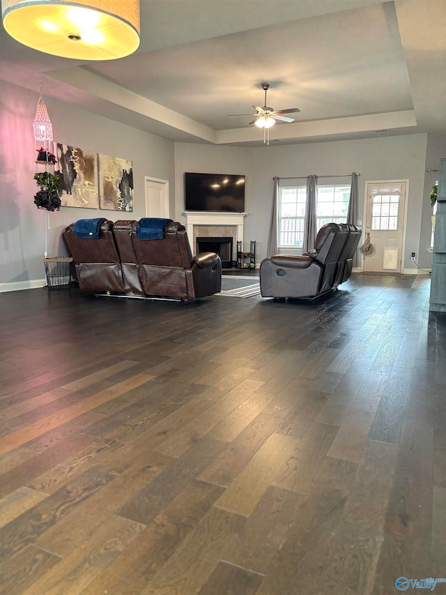 living room with ceiling fan, a raised ceiling, dark wood-type flooring, and a tile fireplace