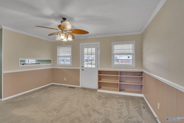 unfurnished room with carpet floors, a wainscoted wall, ornamental molding, and a wealth of natural light