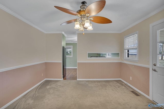 spare room with ceiling fan, carpet floors, visible vents, baseboards, and ornamental molding