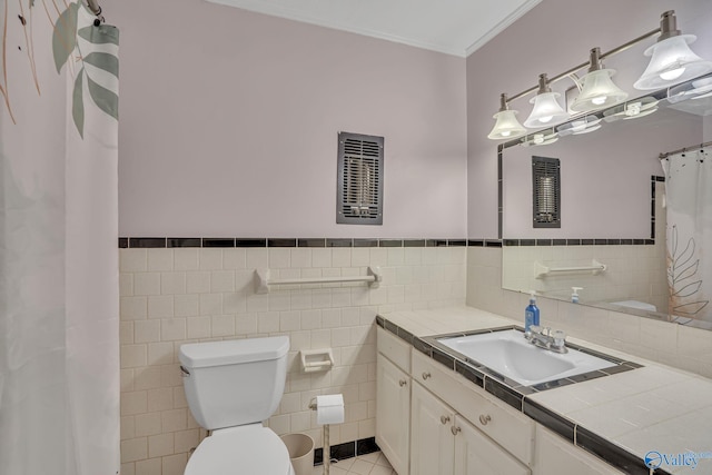 bathroom with wainscoting, toilet, ornamental molding, vanity, and tile walls