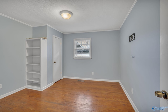 unfurnished bedroom with wood-type flooring, visible vents, ornamental molding, a textured ceiling, and baseboards