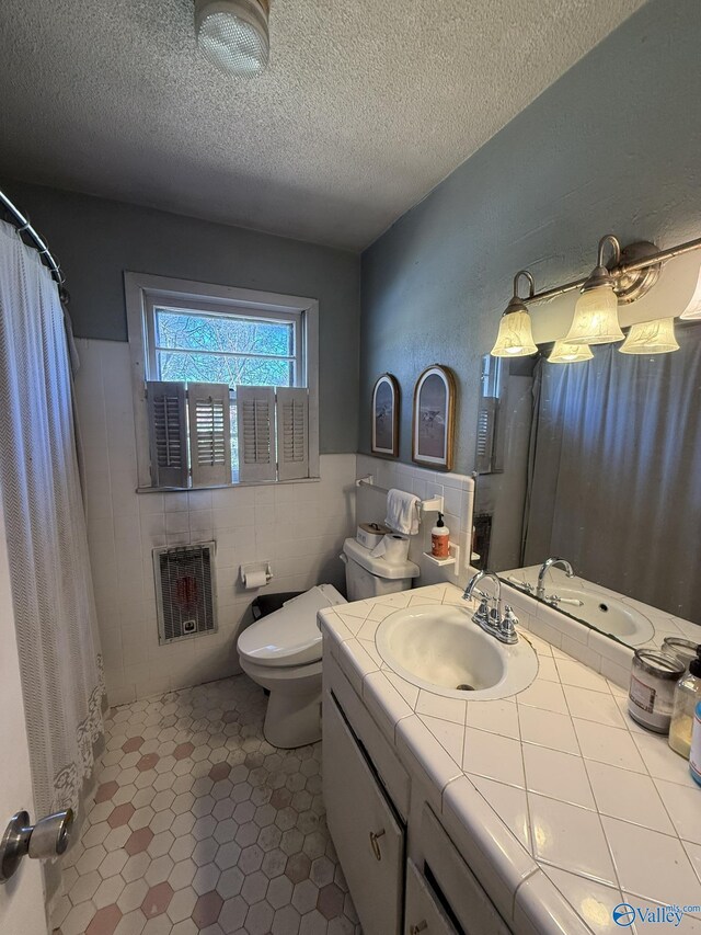 full bath featuring toilet, tile patterned floors, a textured ceiling, vanity, and tile walls