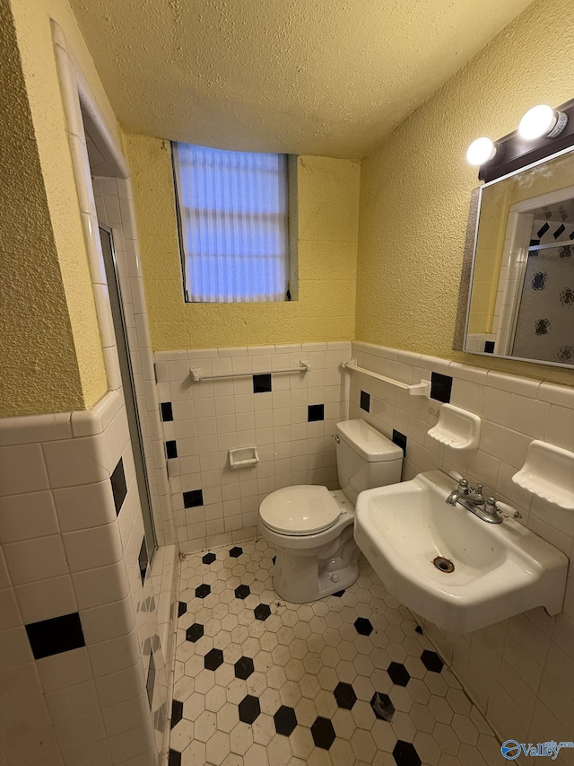 full bathroom with a stall shower, a textured wall, toilet, a textured ceiling, and a sink