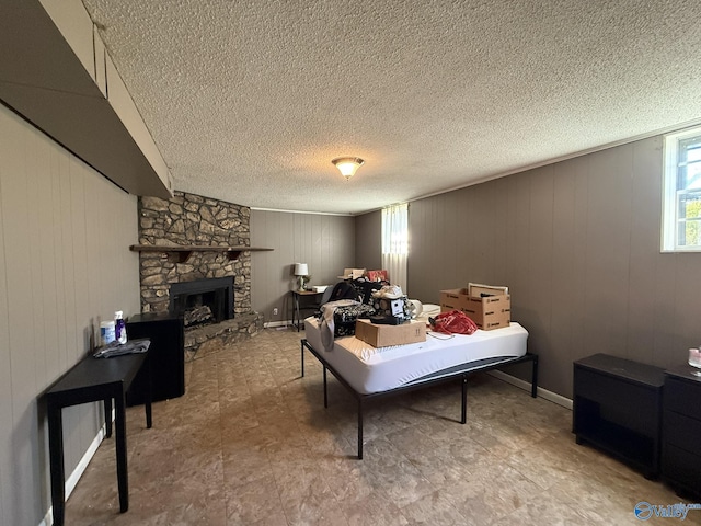 interior space with a textured ceiling, a stone fireplace, and baseboards