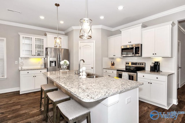 kitchen with decorative light fixtures, a sink, appliances with stainless steel finishes, an island with sink, and glass insert cabinets