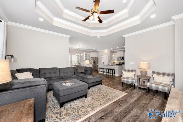 living area with dark wood-type flooring, a raised ceiling, ornamental molding, and ceiling fan with notable chandelier