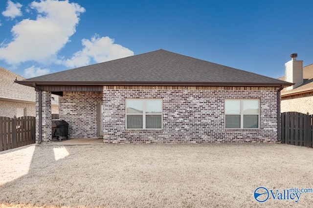 back of house featuring brick siding, fence, and roof with shingles