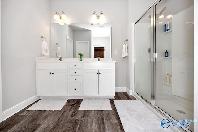 bathroom featuring double vanity, a shower stall, baseboards, and wood finished floors