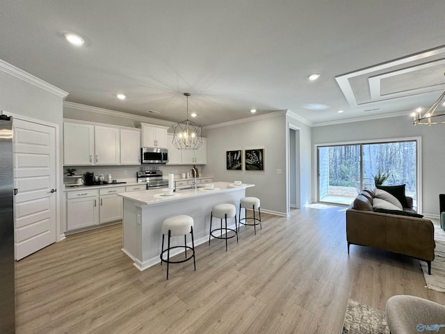 kitchen featuring white cabinets, stainless steel appliances, hanging light fixtures, and an island with sink