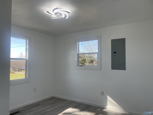 empty room with plenty of natural light, electric panel, baseboards, and wood finished floors