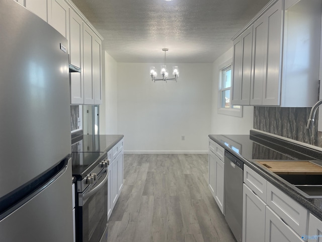 kitchen featuring a notable chandelier, stainless steel appliances, dark countertops, a textured ceiling, and light wood-type flooring