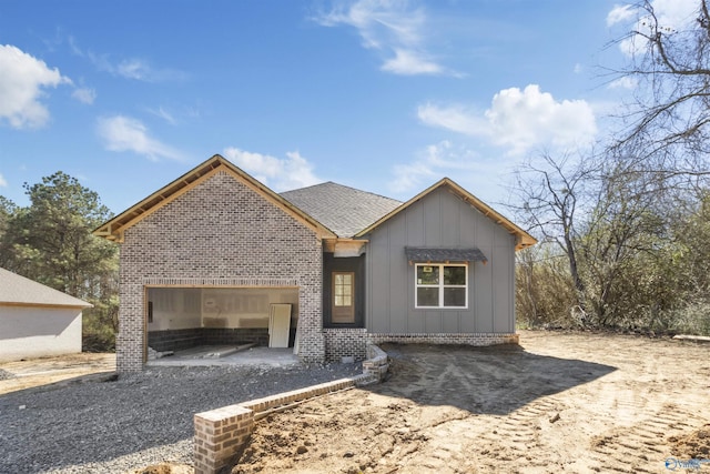 view of front of home with board and batten siding, brick siding, a garage, and roof with shingles