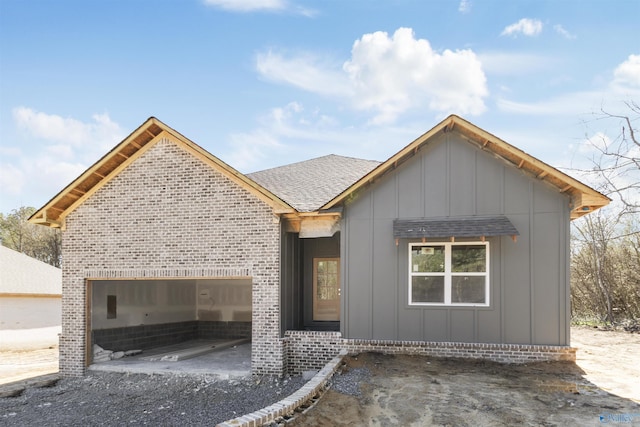 view of front of home with board and batten siding, brick siding, a shingled roof, and an attached garage