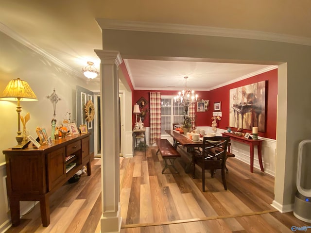 dining space with decorative columns, crown molding, an inviting chandelier, and light wood-type flooring