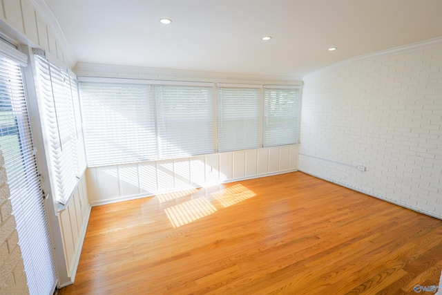 empty room with brick wall, crown molding, and light wood-type flooring