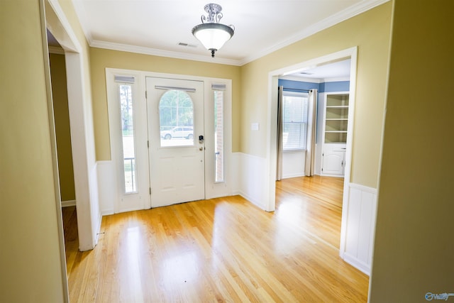 foyer with a wainscoted wall, plenty of natural light, light wood finished floors, crown molding, and a decorative wall