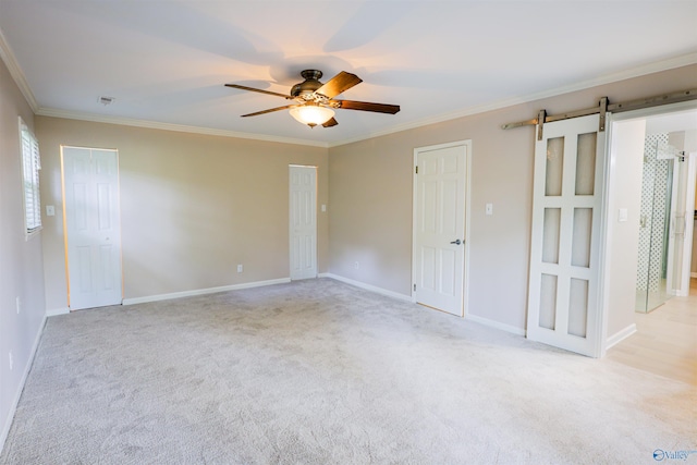 empty room featuring a barn door, a ceiling fan, crown molding, light carpet, and baseboards