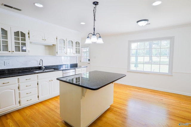 kitchen with a sink, ornamental molding, white dishwasher, glass insert cabinets, and a kitchen island