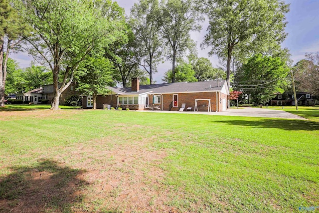 back of house featuring a chimney, brick siding, and a yard