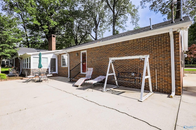 back of house featuring a patio, brick siding, a chimney, and entry steps