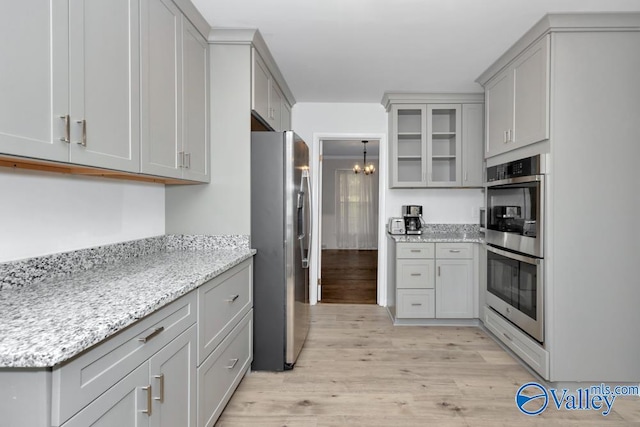 kitchen with gray cabinets, stainless steel appliances, light stone counters, and light hardwood / wood-style flooring