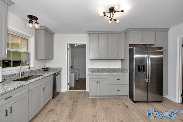 kitchen with light stone countertops, sink, light wood-type flooring, and appliances with stainless steel finishes