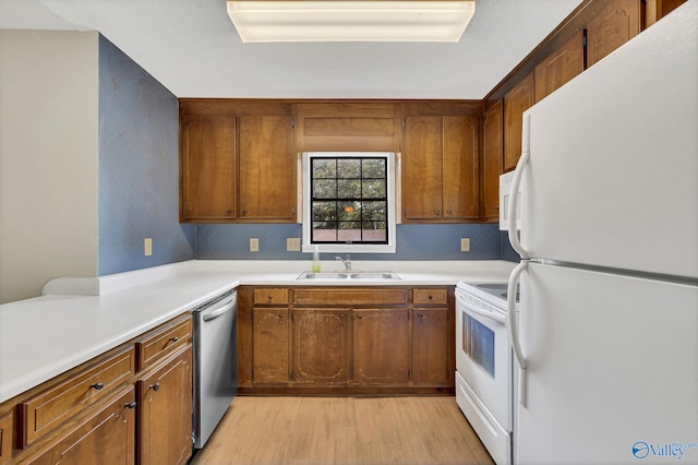 kitchen with light wood-type flooring, white appliances, kitchen peninsula, and sink