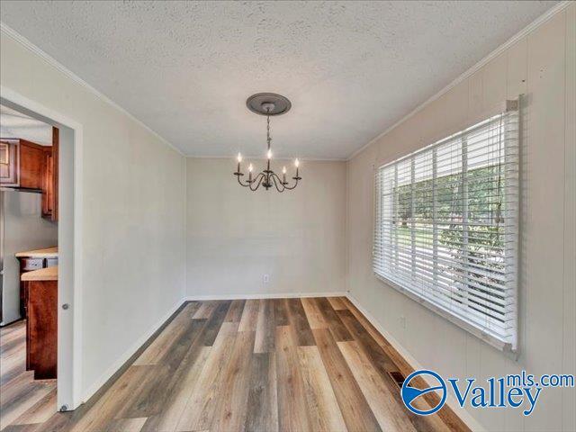 unfurnished dining area with a chandelier, wood finished floors, a textured ceiling, crown molding, and baseboards