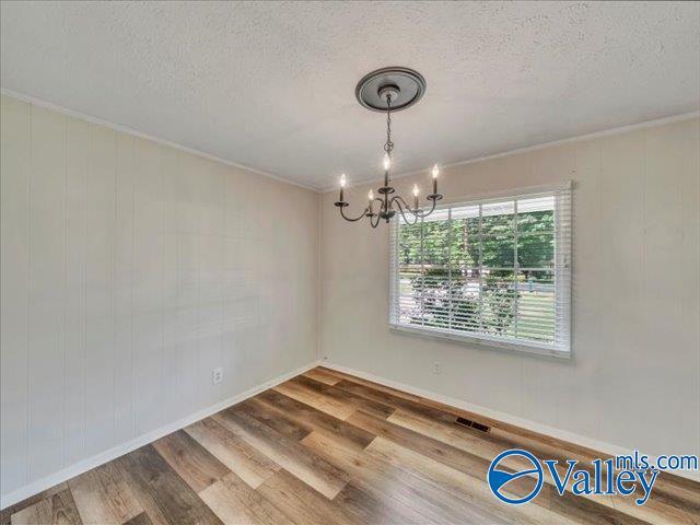 spare room with a chandelier, wood finished floors, a textured ceiling, ornamental molding, and baseboards