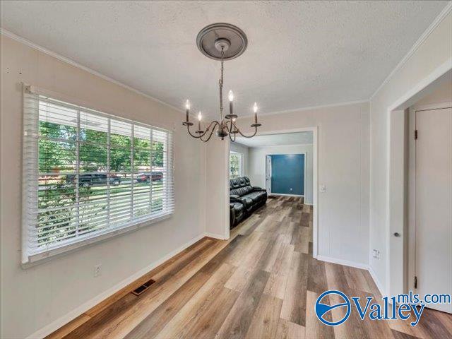 unfurnished dining area with crown molding, a chandelier, a textured ceiling, wood finished floors, and baseboards