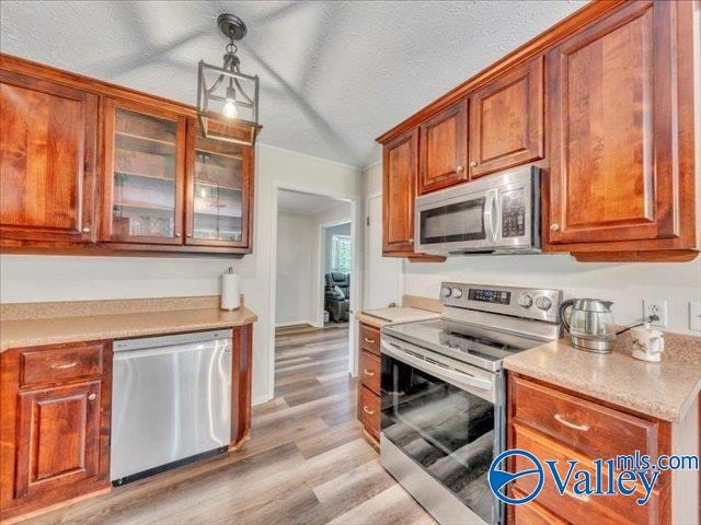 kitchen with stainless steel appliances, light wood finished floors, light countertops, pendant lighting, and a textured ceiling